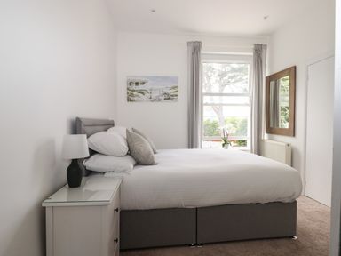 A bedroom with a double bed bedside table and lamp window with curtains and a mirror on the wall at Apartment at Morningside Hotel in Torquay