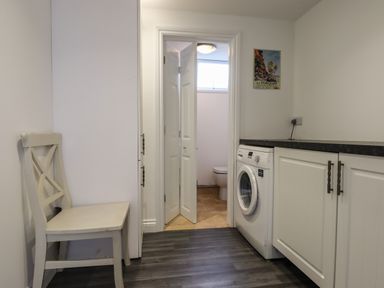 A laundry room with a white chair washing machine and cabinets with a door open to a small bathroom at Apartment at Morningside Hotel in Torquay
