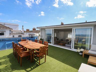 A rooftop terrace with wooden dining table and chairs and sliding glass doors leading to a living room at Apartment at Morningside Hotel in Torquay
