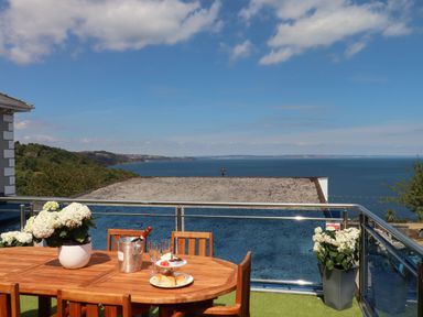An outdoor wooden table with chairs a potted plant ice bucket glasses and a plate of food on a balcony overlooking the sea at Apartment at Morningside Hotel in Torquay