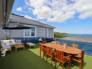An outdoor terrace with a wooden dining table, chairs, a lounge sofa set, and a view of the sea at Apartment at Morningside Hotel in Torquay