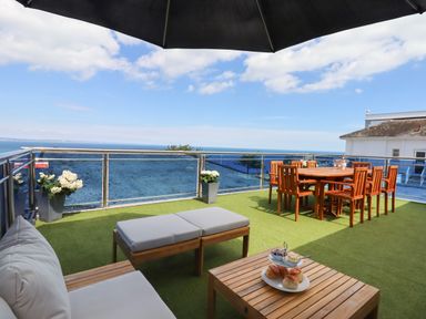 An outdoor terrace with wooden seating and dining table overlooking the ocean at Apartment at Morningside Hotel in Torquay