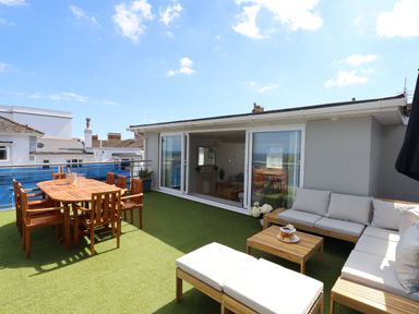 An outdoor terrace with wooden dining table and chairs and cushioned seating at Apartment at Morningside Hotel in Torquay