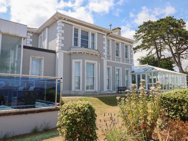 A large gray and white house with many windows and a glass conservatory surrounded by garden plants at Apartment at Morningside Hotel in Torquay