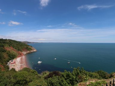A coastal landscape with a beach boats and greenery at Apartment at Morningside Hotel in Torquay
