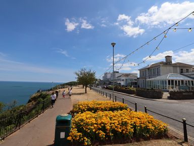 A coastal walkway with people walking near yellow flowers and buildings by the sea at Apartment at Morningside Hotel in Torquay