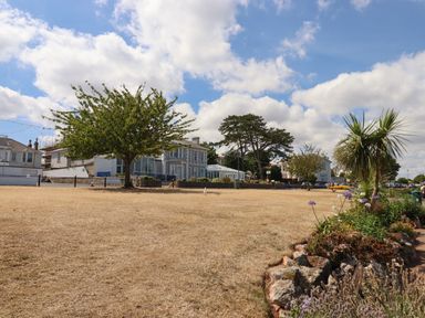 An outdoor grassy area with a tree in the middle and buildings in the background at Apartment at Morningside Hotel in Torquay