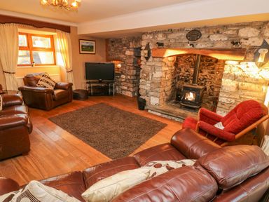 A living room with leather sofas a red armchair a stone fireplace with a wood burner a television and a window with curtains at Pant Teg Farm in Carmarthen