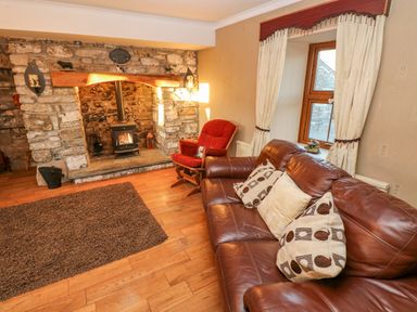 A living room with a stone fireplace wood stove a brown leather sofa and a red armchair at Pant Teg Farm in Carmarthen
