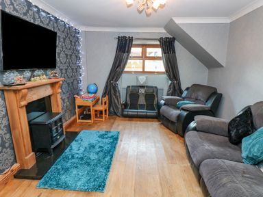 A living room with gray sofas a wooden fireplace and a television on the wall at Pant Teg Farm in Carmarthen