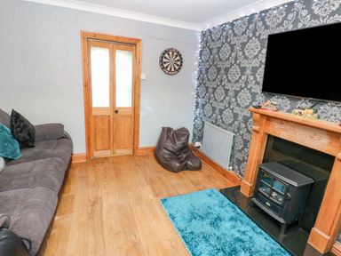 A living room with a gray sofa pillows a blue rug a fireplace a dartboard and a bean bag at Pant Teg Farm in Carmarthen