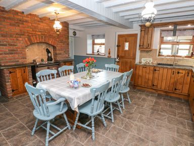 A kitchen with a dining table and blue chairs near wooden cabinets and a brick fireplace at Pant Teg Farm in Carmarthen