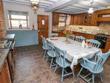 A kitchen with wooden cabinets a dining table with blue chairs and a vase of flowers at Pant Teg Farm Carmarthen
