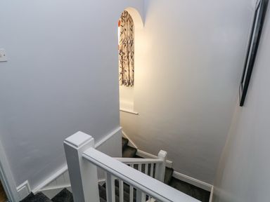 A staircase with white railing and dark carpet leading down with an arched window with curtains at Pant Teg Farm in Carmarthen