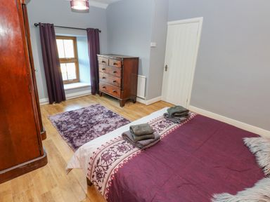 A bedroom with a bed, wooden chest of drawers, purple curtains, and a purple rug at Pant Teg Farm in Carmarthen