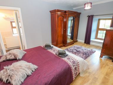 A bedroom with a bed covered in purple bedding two windows purple curtains wooden wardrobe and a purple rug at Pant Teg Farm in Carmarthen