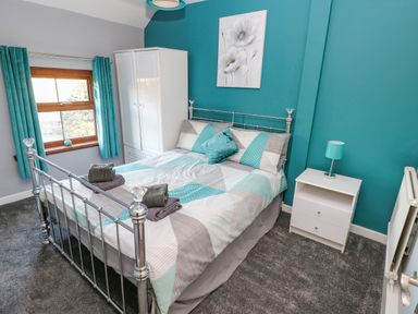 A bedroom with a metal bed frame blue and gray bedding a white wardrobe a bedside table with a lamp and blue curtains at Pant Teg Farm in Carmarthen