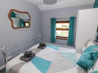 A bedroom with a bed, folded towels on the bed, a window with teal curtains and a wall mirror at Pant Teg Farm in Carmarthen