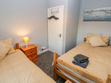A bedroom with two single beds a wooden nightstand with a lamp and a door with hangers at Pant Teg Farm in Carmarthen