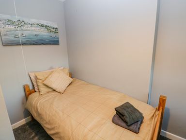 A small bedroom with a single bed beige bedding two pillows a painting on the wall and folded towels on the bed at Pant Teg Farm in Carmarthen
