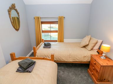 A bedroom with two single beds a wooden nightstand with a lamp yellow curtains and a decorative wall mirror at Pant Teg Farm in Carmarthen