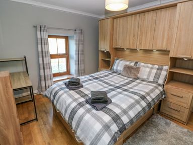A bedroom with a double bed and built-in wooden cabinets with a window with curtains at Pant Teg Farm in Carmarthen