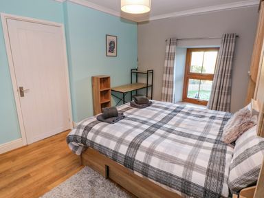 A bedroom with a bed a window with curtains a desk shelving unit and a door at Pant Teg Farm in Carmarthen