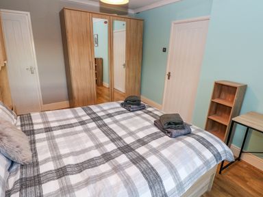 A bedroom with a bed with checkered bedding two doors a wooden wardrobe with mirrors a small wooden shelf and a table at Pant Teg Farm in Carmarthen