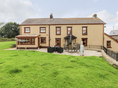 A patio with outdoor furniture and a grassy lawn in front of a house at Pant Teg Farm in Carmarthen
