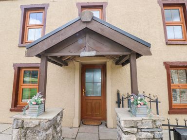 A front door with a wooden porch and stone pillars with flower pots at Pant Teg Farm in Carmarthen
