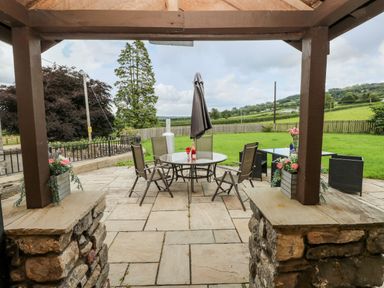 An outdoor patio with a round table and chairs under a wooden pergola at Pant Teg Farm in Carmarthen