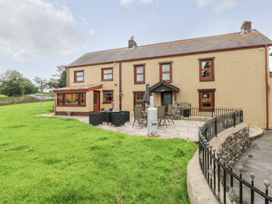 The rear of a two story house with a paved patio garden furniture and a lawn at Pant Teg Farm in Carmarthen
