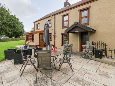 An outdoor patio area with a round table and chairs next to a house with beige walls and wooden framed windows at Pant Teg Farm in Carmarthen