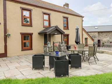 A patio with outdoor furniture including glass tables and chairs outside a beige building at Pant Teg Farm in Carmarthen
