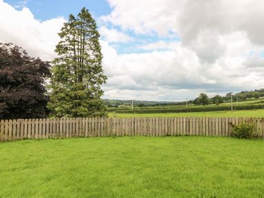 A grassy backyard with a wooden picket fence trees and fields beyond at Pant Teg Farm Carmarthen