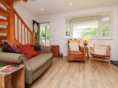 A living room with a sofa, armchair, wooden chair, side table with a lamp, and wooden staircase at Barleside in Dulverton