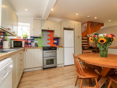 A kitchen with colorful tiled backsplash wooden cabinets white appliances wooden table with chairs and flowers in a vase at Barleside in Dulverton