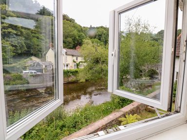 A view through open windows showing a river with houses and trees at Barleside in Dulverton