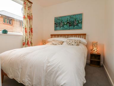 A bedroom with a double bed white bedding two cushions wooden headboard side tables with lamps window with floral curtains painting above the bed at Barleside in Dulverton
