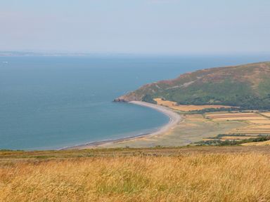 A coastal landscape with a curved beach ocean hills and grassy fields at Barleside in Dulverton