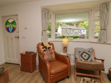 A sitting area with two chairs a small table with a lamp a basket with firewood and a window showing a house outside at Barleside in Dulverton