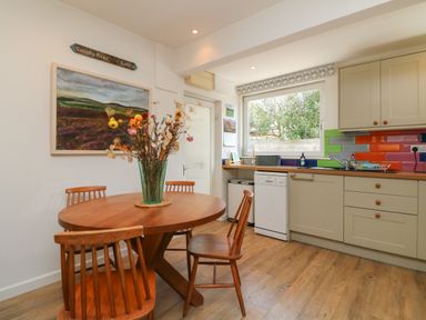 A kitchen with a wooden round table and chairs and colorful tiled backsplash at Barleside in Dulverton