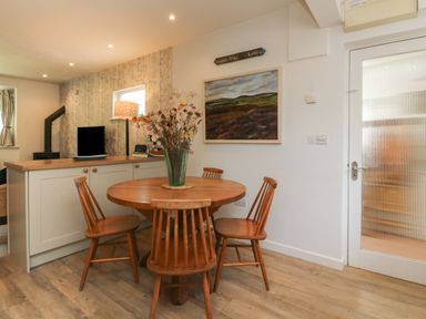 A dining area with a round wooden table and four chairs next to a kitchen counter and a glass door at Barleside in Dulverton