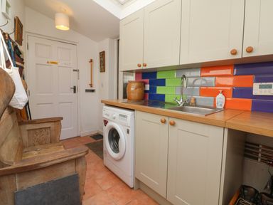 A utility room with a wooden bench a washing machine a sink with colorful tiles on the wall and cabinets above at Barleside in Dulverton