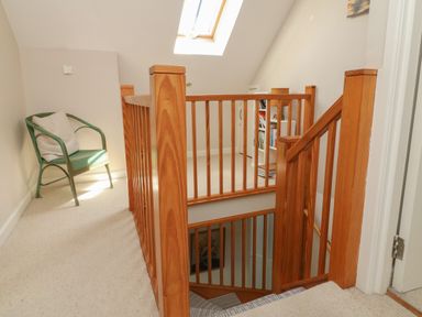 A hallway with a wooden staircase a green chair with a cushion and a skylight at Barleside in Dulverton