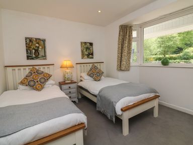 A bedroom with two single beds a bedside table with a lamp paintings on the wall and a window with a view of trees at Barleside in Dulverton