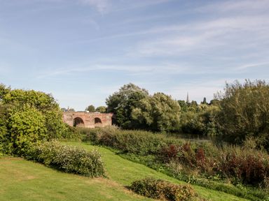 A river with trees and bushes along the bank and a stone bridge over the river at Steel Works Farm in Gorsley