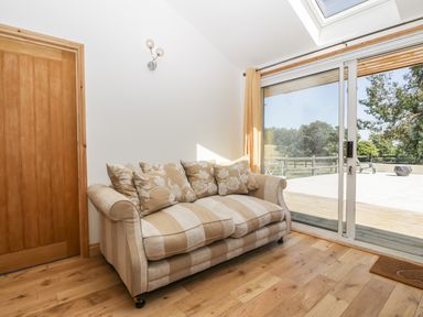 A beige striped sofa with patterned cushions next to a sliding glass door and wooden door on a wooden floor