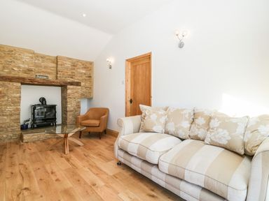 A living room with a striped sofa, armchair, glass coffee table, wood stove in a stone fireplace at Steel Works Farm in Gorsley