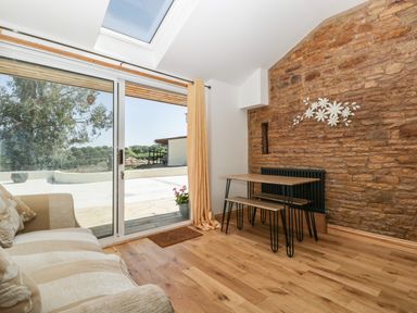 A room with a sofa, wooden table with benches, stone wall, sliding glass door, and skylight at Steel Works Farm in Gorsley